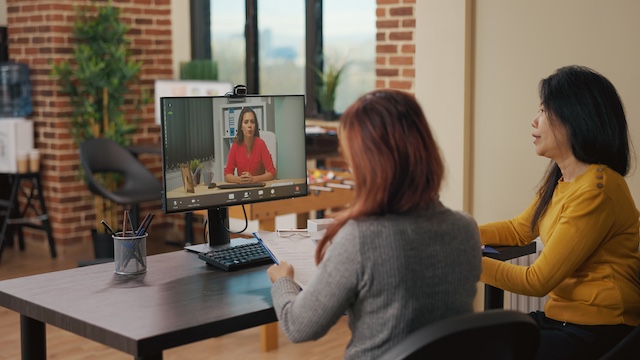 Two female managers sit side-by-side to interview a female candidate using a video conference call