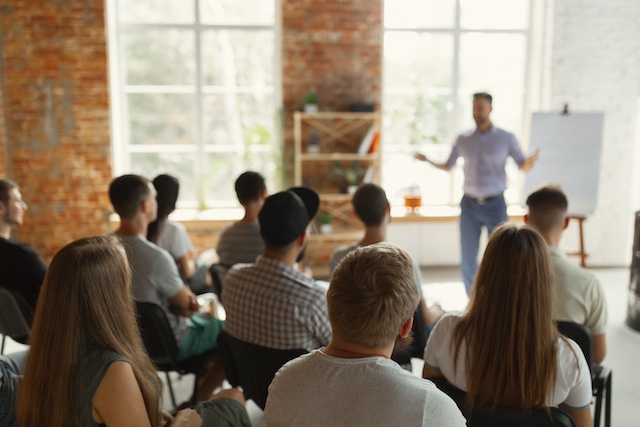 An audience of employees watches as a male trainer presents to them