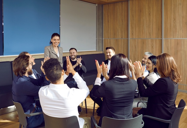 A group of employees applaud a female team leader in a meeting room
