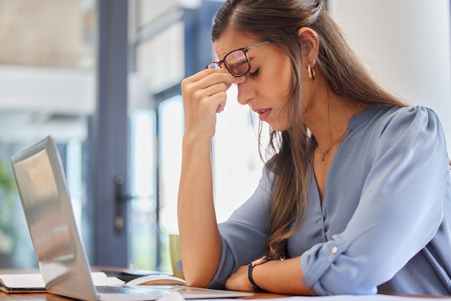 A female employee rubs her head in stress while sitting at her desk with laptop