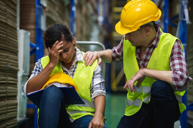 A male factory worker consoles a female coworker on the plant floor