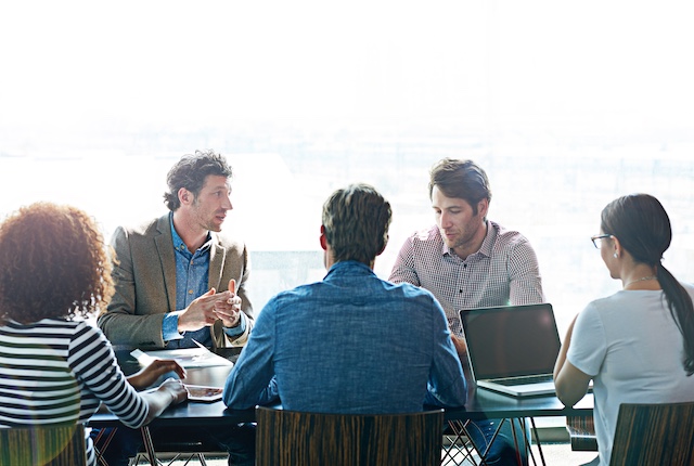 Five team members sit at a conference table for a serious meeting