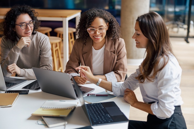 three diverse coworkers sit at a table in an office working on a project