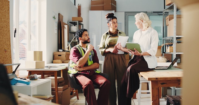 A retail manager meets with two employees in a stockroom
