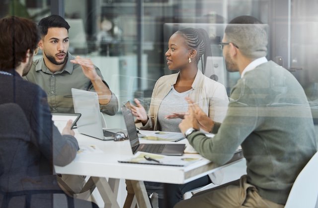 Teammates collaborate in a meeting room seen through glass walls