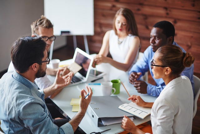 A group of diverse colleagues meet around a table at work